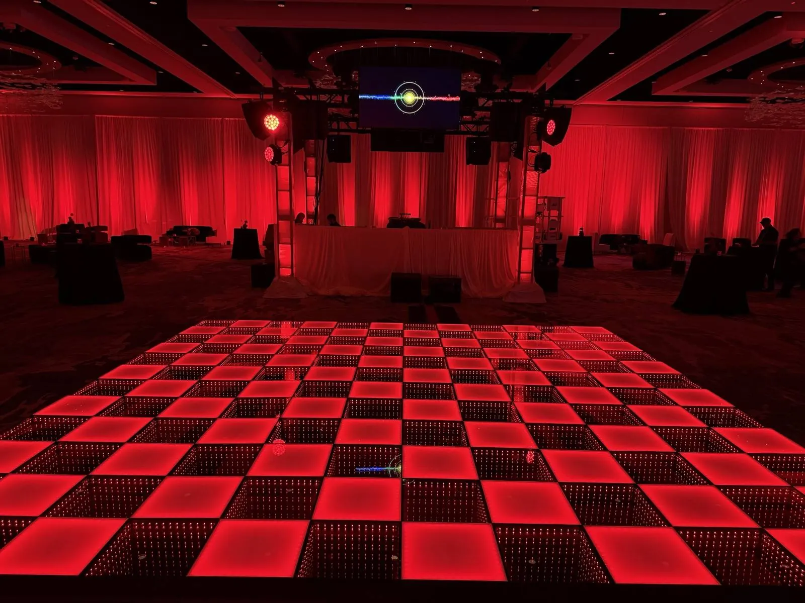 Red checkered frosted and infinity LED dance floor matching red uplighting and drapery in a hotel ballroom