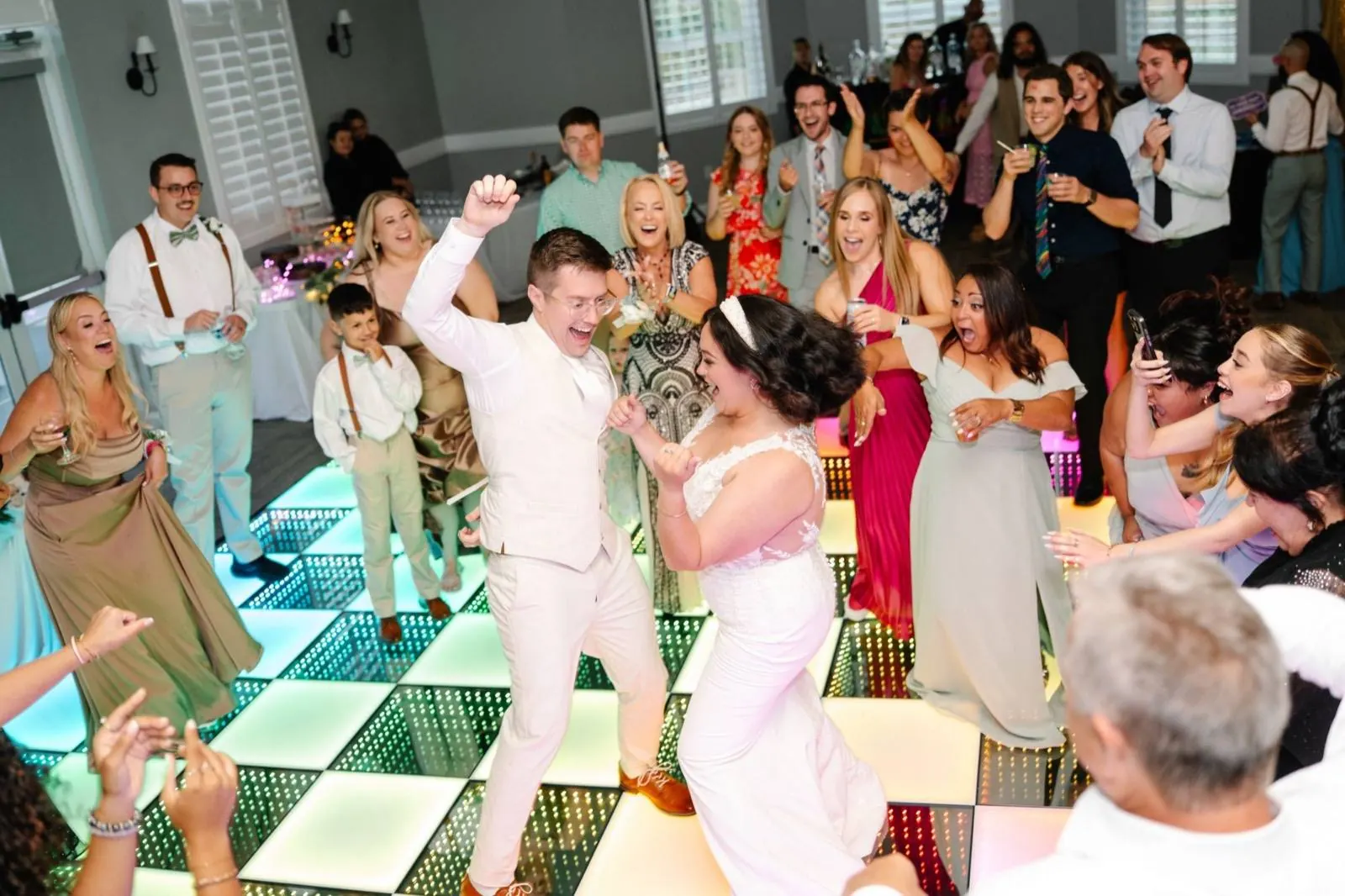 Bride and groom dancing on a checkered frosted and infinity LED dance floor as cheering wedding guests crowd around them